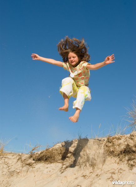 Kind springt van een duin